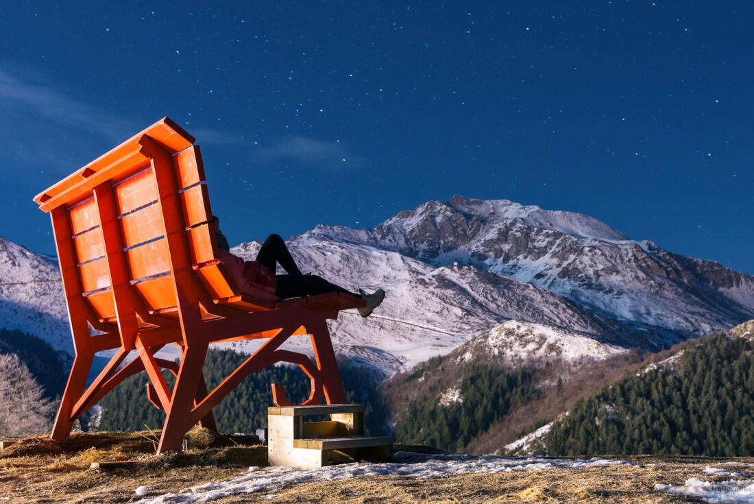 En kvinde sidder på en stor bænk i Prato Nevoso-bjergene om natten i Piemonte-alperne i Italien