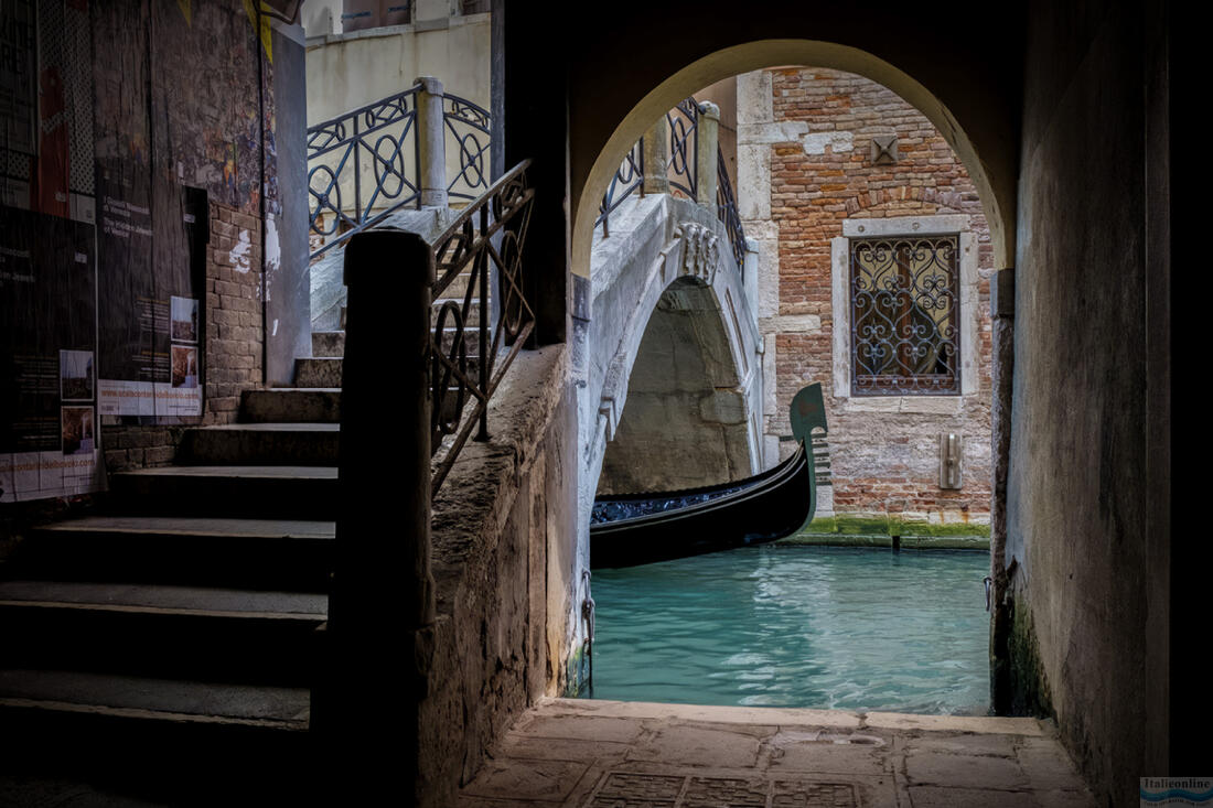 Гондола проходит под небольшим мостом в Венеции.